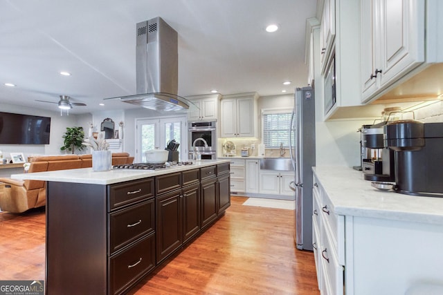 kitchen featuring light wood-type flooring, white cabinetry, stainless steel appliances, and extractor fan