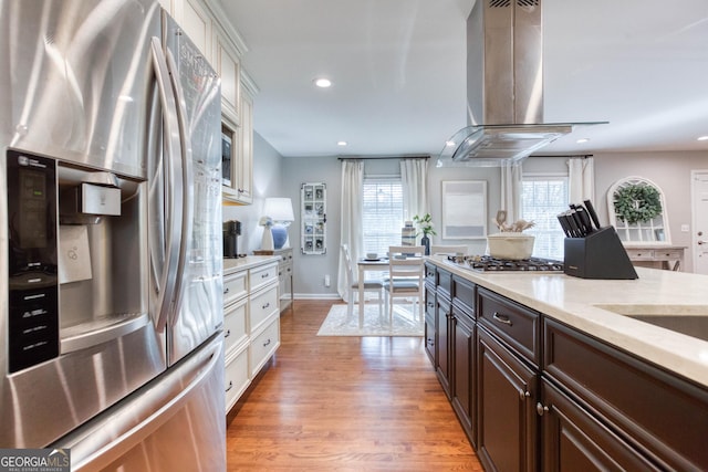 kitchen featuring appliances with stainless steel finishes, dark brown cabinets, light hardwood / wood-style floors, light stone counters, and island exhaust hood