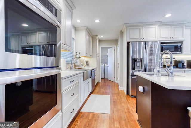 kitchen with tasteful backsplash, stainless steel appliances, washer and dryer, light hardwood / wood-style flooring, and white cabinetry