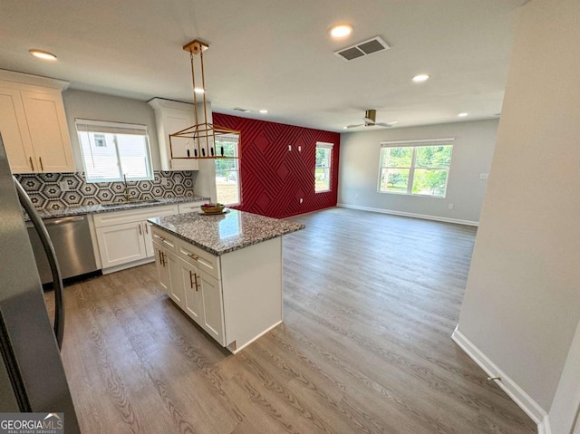 kitchen featuring light stone countertops, white cabinetry, dishwasher, and pendant lighting