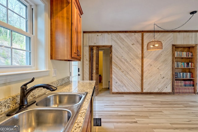 kitchen with crown molding, sink, wooden walls, decorative light fixtures, and a healthy amount of sunlight