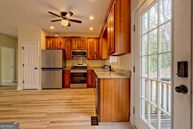 kitchen featuring light stone countertops, stainless steel appliances, ceiling fan, sink, and light hardwood / wood-style flooring