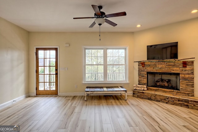 unfurnished living room with ceiling fan, a stone fireplace, and light hardwood / wood-style flooring