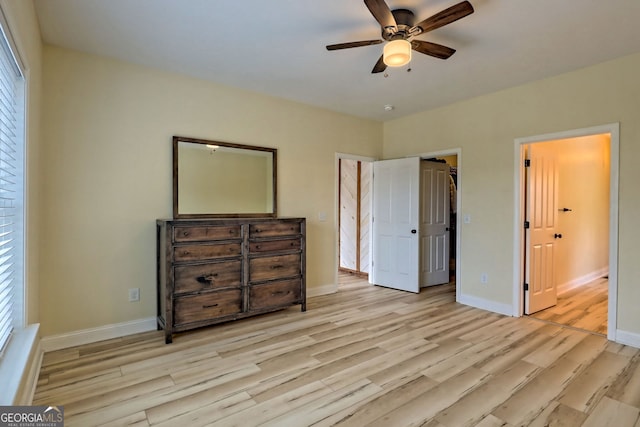 bedroom featuring a walk in closet, ceiling fan, a closet, and light wood-type flooring