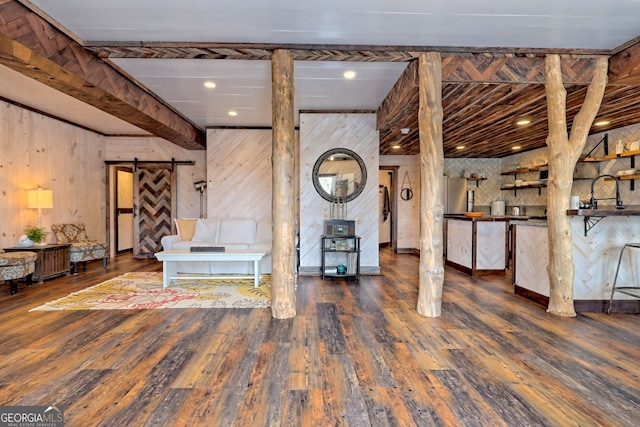 unfurnished living room with a barn door, wood walls, and dark hardwood / wood-style flooring