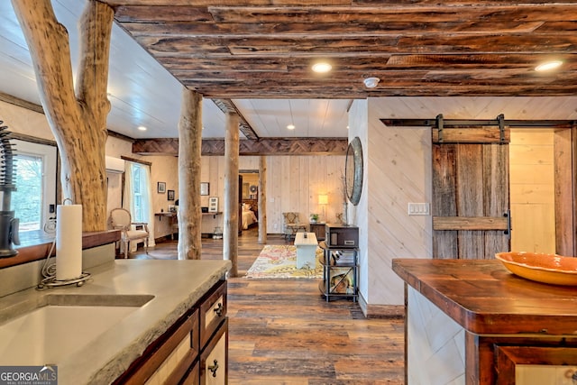 kitchen with a barn door, dark hardwood / wood-style flooring, wooden ceiling, and wooden walls