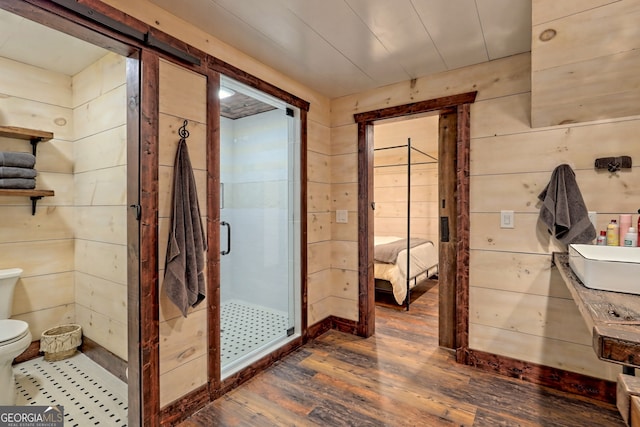 bathroom featuring wooden walls, wood-type flooring, a shower with shower door, and toilet