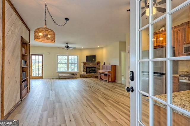 unfurnished living room with a stone fireplace, ceiling fan, and light hardwood / wood-style floors