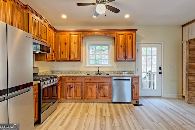 kitchen with light stone countertops, stainless steel appliances, ceiling fan, sink, and light hardwood / wood-style floors