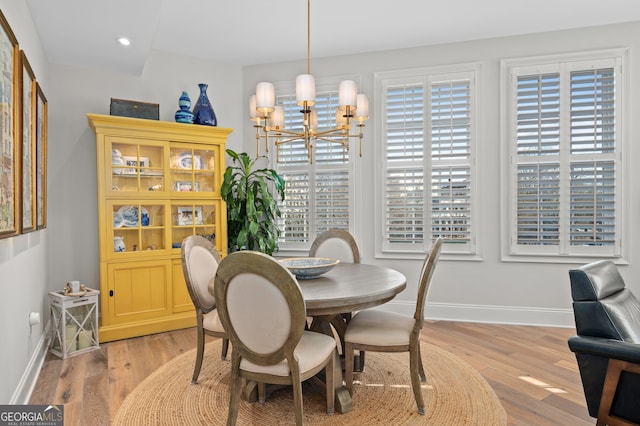 dining area with light hardwood / wood-style floors, a wealth of natural light, and an inviting chandelier