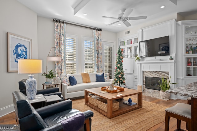 living room featuring a high end fireplace, light wood-type flooring, and ceiling fan