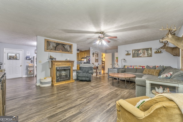 living room featuring a ceiling fan, dark wood-style flooring, a fireplace, and a textured ceiling