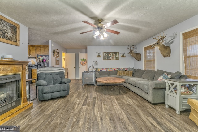 living area with a fireplace with raised hearth, ceiling fan, a textured ceiling, and wood finished floors