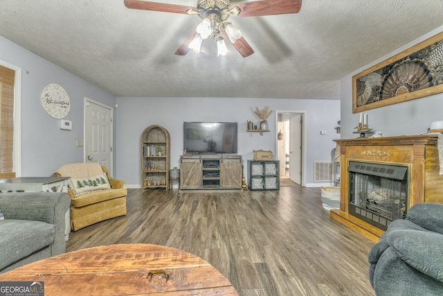 living room featuring a fireplace with raised hearth, a textured ceiling, wood finished floors, visible vents, and baseboards