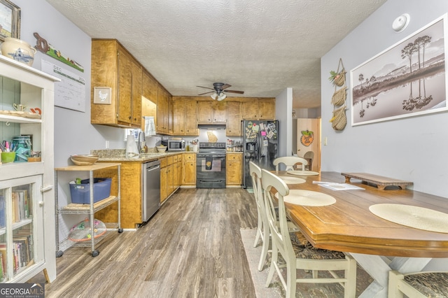 kitchen featuring a textured ceiling, dark wood-style flooring, a sink, brown cabinets, and black appliances