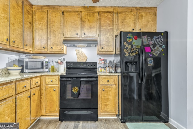 kitchen featuring brown cabinets, light countertops, light wood-type flooring, under cabinet range hood, and black appliances