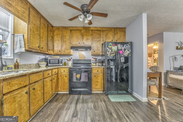 kitchen featuring dark wood-type flooring, brown cabinetry, under cabinet range hood, and black appliances