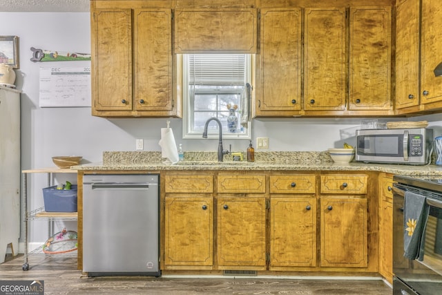 kitchen with brown cabinets, appliances with stainless steel finishes, dark wood finished floors, and a sink