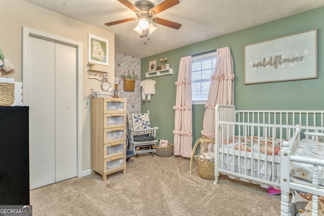 carpeted bedroom featuring a textured ceiling, ceiling fan, a closet, and a nursery area