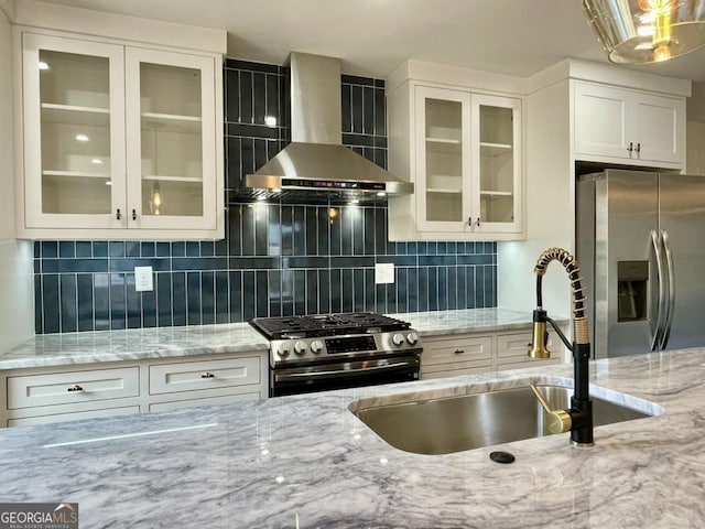 kitchen featuring sink, wall chimney exhaust hood, light stone countertops, appliances with stainless steel finishes, and white cabinetry