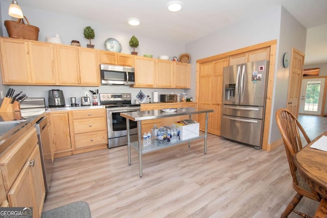 kitchen with light brown cabinetry, stainless steel appliances, a kitchen island, and light hardwood / wood-style floors