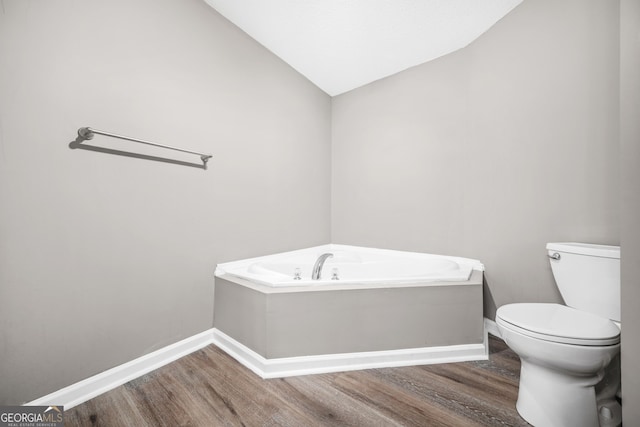 bathroom with a tub, hardwood / wood-style floors, lofted ceiling, and toilet