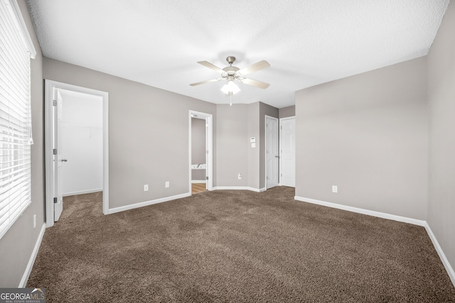 unfurnished bedroom with ensuite bath, ceiling fan, a textured ceiling, a walk in closet, and dark carpet