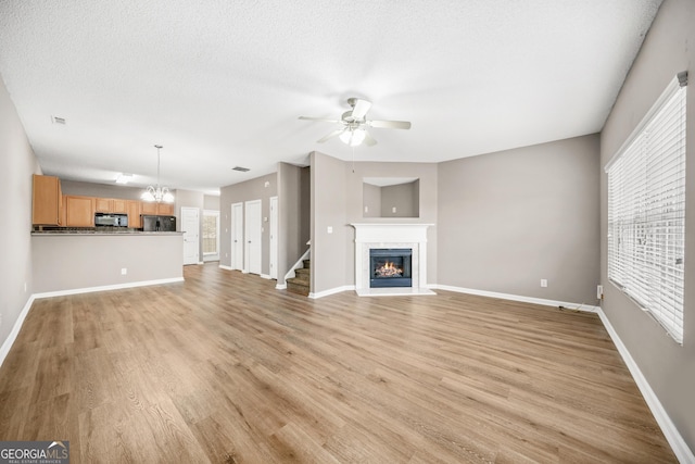 unfurnished living room with a textured ceiling, light hardwood / wood-style flooring, a healthy amount of sunlight, and ceiling fan with notable chandelier