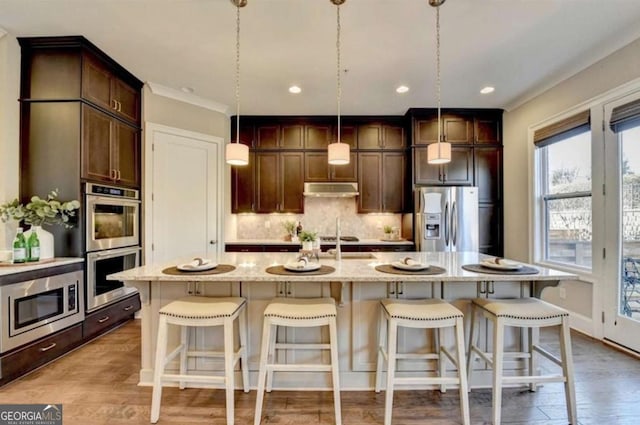 kitchen with a center island with sink, light stone counters, stainless steel appliances, and hanging light fixtures