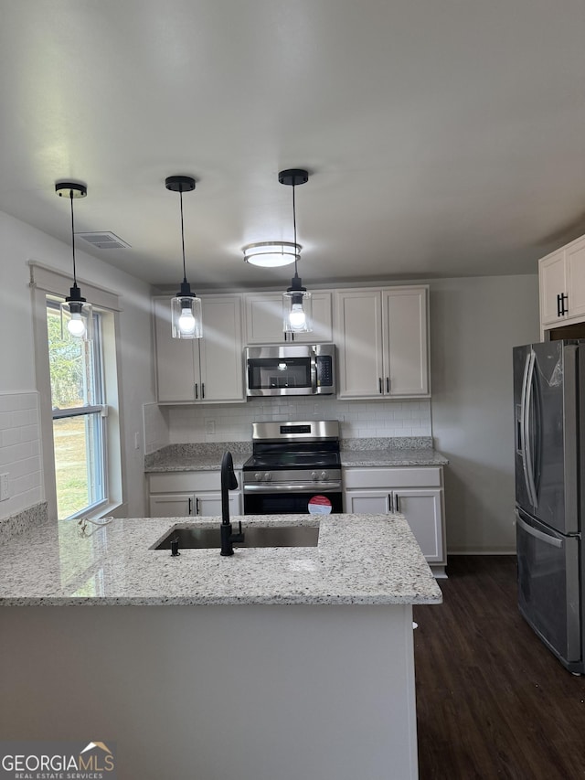 kitchen featuring sink, light stone counters, hanging light fixtures, appliances with stainless steel finishes, and kitchen peninsula