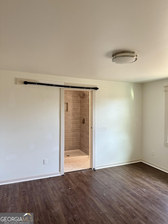 unfurnished bedroom featuring a barn door, dark wood-type flooring, and connected bathroom