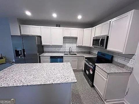 kitchen featuring sink, white cabinetry, light stone counters, decorative backsplash, and black appliances