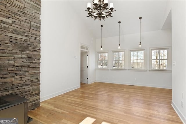 unfurnished living room featuring light wood-type flooring, high vaulted ceiling, and an inviting chandelier