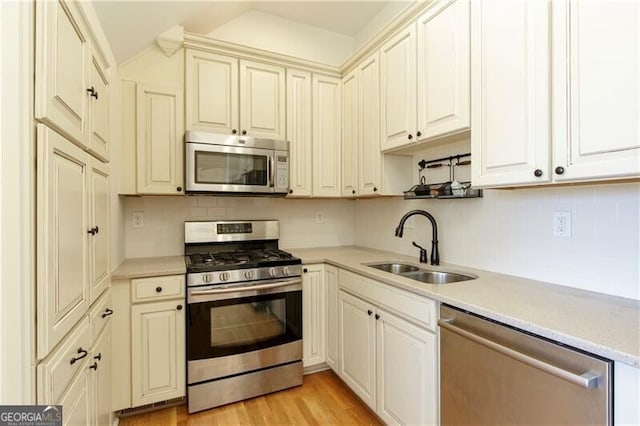kitchen featuring appliances with stainless steel finishes, backsplash, light hardwood / wood-style floors, and sink