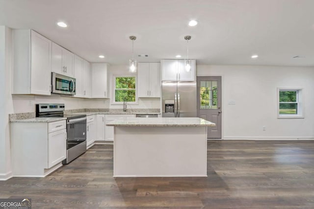 kitchen with light stone counters, stainless steel appliances, a kitchen island, white cabinetry, and hanging light fixtures