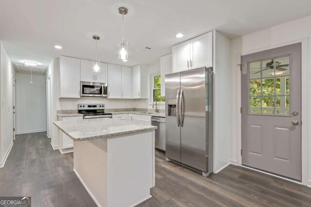 kitchen featuring hanging light fixtures, a kitchen island, light stone counters, white cabinets, and appliances with stainless steel finishes