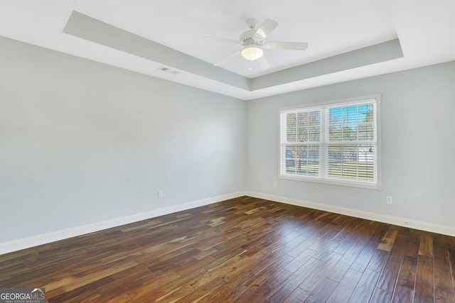 empty room featuring a raised ceiling, ceiling fan, and dark wood-type flooring