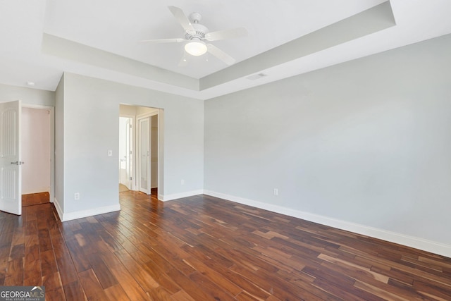 spare room with dark hardwood / wood-style flooring, ceiling fan, and a raised ceiling