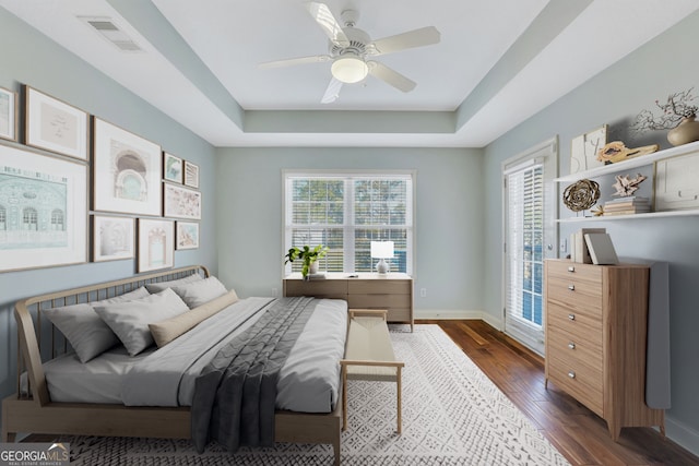 bedroom with ceiling fan, dark hardwood / wood-style flooring, and a tray ceiling