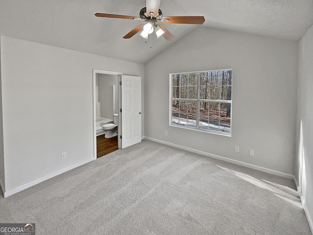 unfurnished bedroom with lofted ceiling, ceiling fan, a textured ceiling, connected bathroom, and light colored carpet