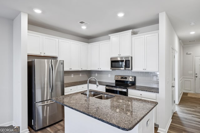 kitchen with appliances with stainless steel finishes, a kitchen island with sink, sink, dark stone countertops, and white cabinets