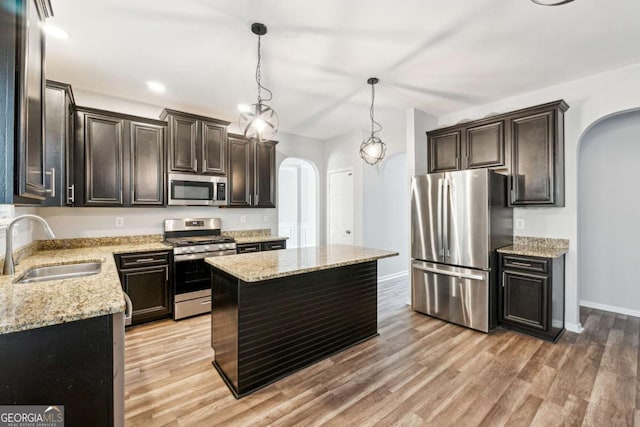 kitchen with appliances with stainless steel finishes, light stone counters, sink, a kitchen island, and hanging light fixtures