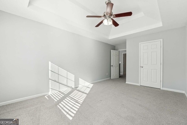 carpeted empty room with ceiling fan and a raised ceiling