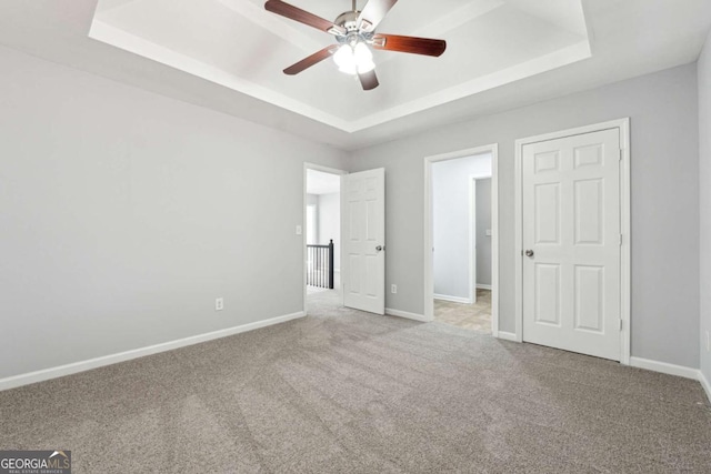 unfurnished bedroom featuring a tray ceiling, ceiling fan, and light carpet