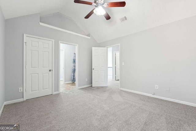 unfurnished bedroom featuring ceiling fan, light colored carpet, connected bathroom, and vaulted ceiling