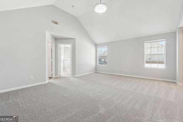 empty room with light colored carpet, vaulted ceiling, and a healthy amount of sunlight