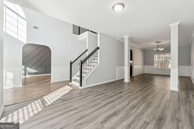 unfurnished living room with wood-type flooring, crown molding, and decorative columns