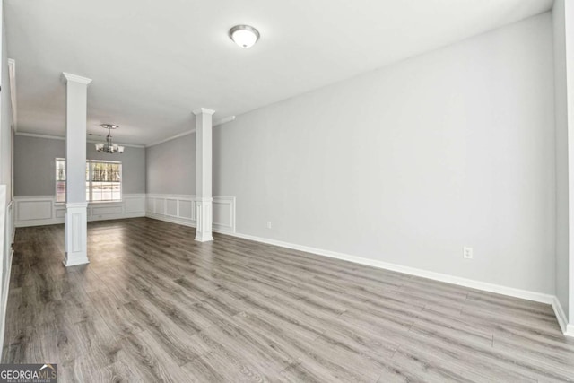 unfurnished living room with decorative columns, ornamental molding, light hardwood / wood-style flooring, and an inviting chandelier