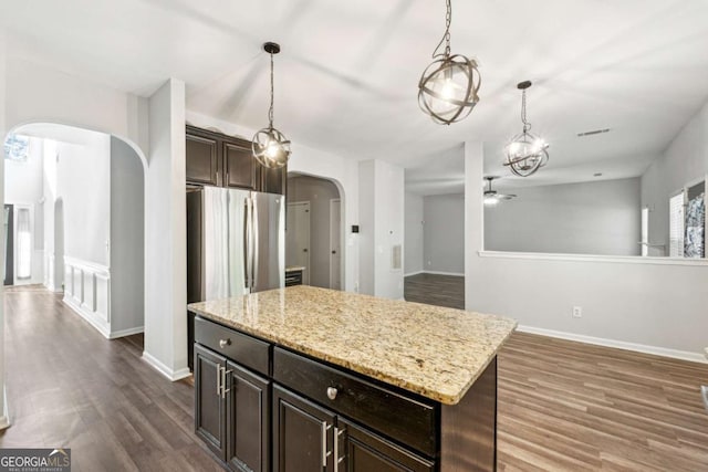 kitchen with dark brown cabinets, a center island, light stone countertops, and ceiling fan