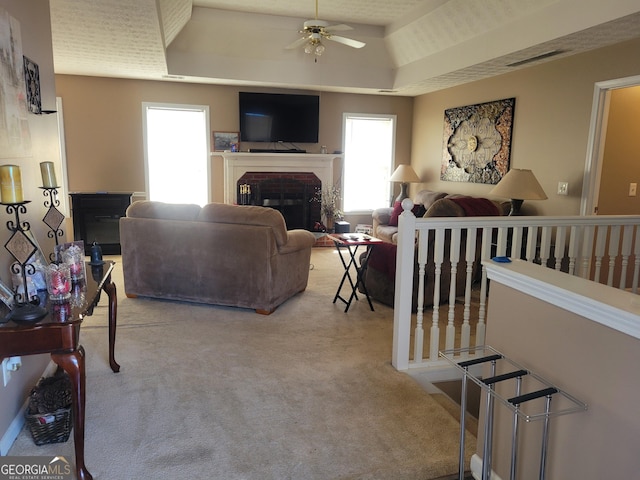 living room with ceiling fan, a raised ceiling, light colored carpet, and a fireplace